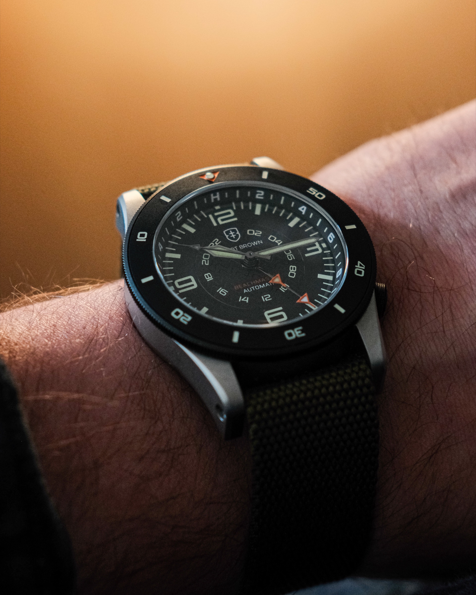 A GMT watch on wrist, warm amber light, olive NATO strap